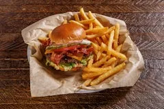 BBQ Ranch Bacon Burger served with crispy golden fries on parchment paper, featuring a grilled beef patty, smoked bacon, melted cheddar, lettuce, tomato, pickle, red onion, and chipotle ranch on a toasted bun.