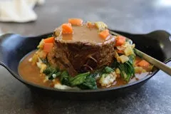 Campfire Pot Roast topped with gravy and vegetables, served with mashed potatoes and sautéed spinach.