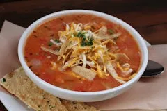 Catering 73 Chicken Tortilla Soup topped with cheddar cheese, tortilla strips, and fresh herbs in a hearty tomato broth.
