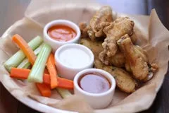Happy Hour 24 Crispy Wings served with celery and carrots, paired with blue cheese, BBQ, and high-altitude hot sauces.