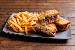 Cuban Sandwich with layers of smoked ham, slow-cooked pork, Swiss cheese, and pickles, served with golden fries.