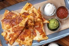 Happy Hour 18 Inside Out Quesadilla filled with melted cheddar and jack cheese in a crispy cheese crust, served with guacamole, sour cream, and housemade salsa.