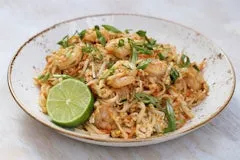 Thai Noodles with shrimp, chicken, tofu, peanuts, bean sprouts, and egg tossed in pad thai sauce with a lime wedge.