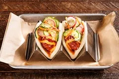 Home 22 Two soft bao buns filled with crispy Korean fried chicken, gochugaru pepper glaze, kimchi aioli, and pickled cucumbers