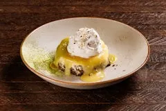 Home 26 Creamy cheesecake with a black sesame crust, topped with tangy yuzu lime curd, matcha tea dust, and a swirl of whipped cream, served on a dessert plate